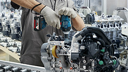 Un travailleur portant un casque et un masque de protection utilise une perceuse sur un échafaudage.