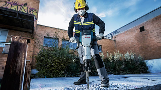 Un travailleur avec un marteau Bosch travaille le béton à l'extérieur.