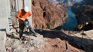 Un travailleur avec un casque utilise un perforateur sur la pente d'un canyon.