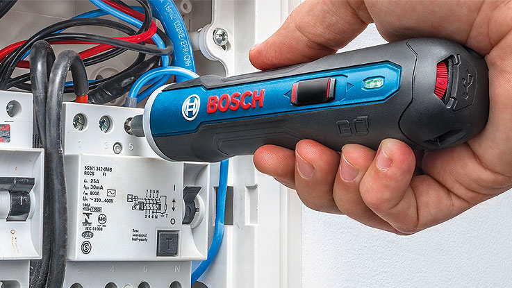 Un probador de voltaje Bosch Professional se sostiene cerca de un cuadro de fusibles.