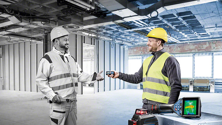 Два строителя в касках безопасности обмениваются инструментами на строительном объекте.