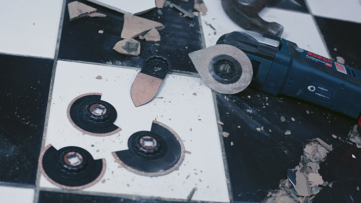 Профессиональный инструмент Bosch лежит на черно-белом полу, окруженный мусором.