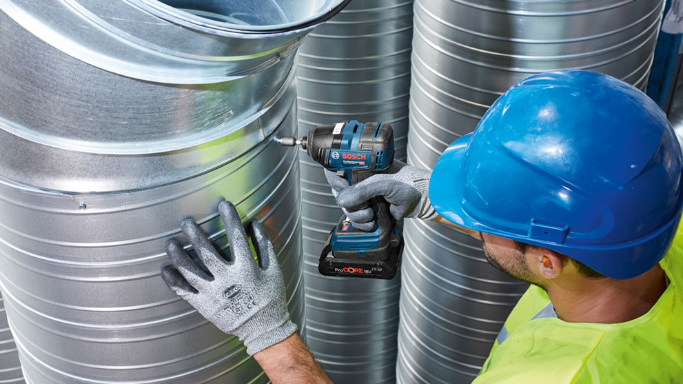 Рабочий с синей дрелью Bosch Professional на металлических трубах.