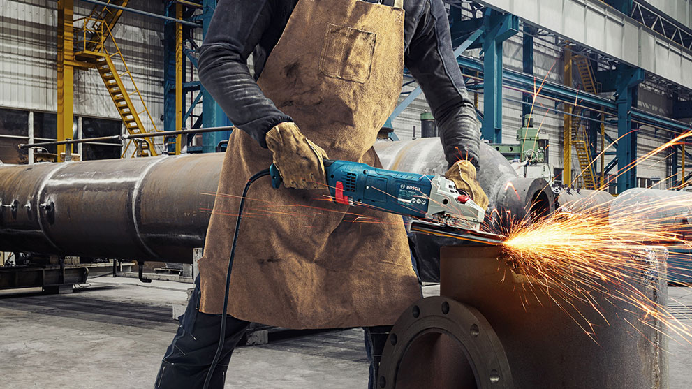 Рабочий с инструментами Bosch Professional режет металл и распыляет искры.