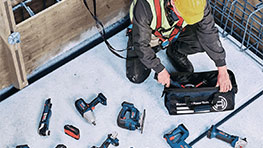 A worker with a helmet sorts Bosch Professional tools on the floor.