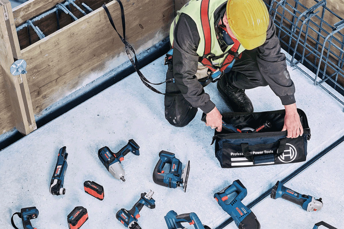 A worker sorts Bosch tools in a black bag on the floor.