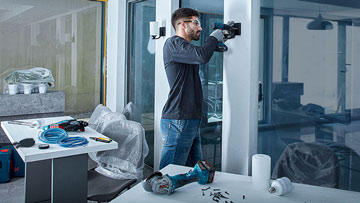 Muž s brýlemi vrtá v moderním kancelářském prostředí.