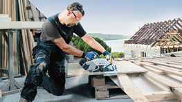 Ремесленник в защитных очках режет дерево на крыше.