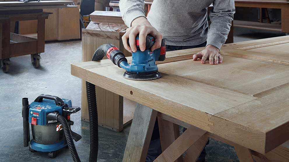 Профессиональный шлифовщик Bosch используется на деревянной доске.