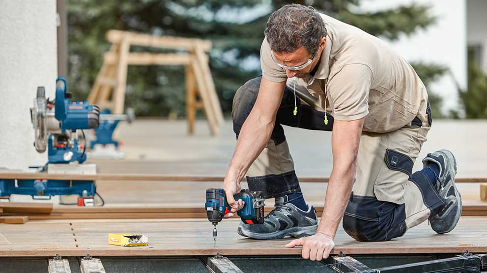 Ремесленник с аккумуляторной дрелью Bosch Professional работает на полу.