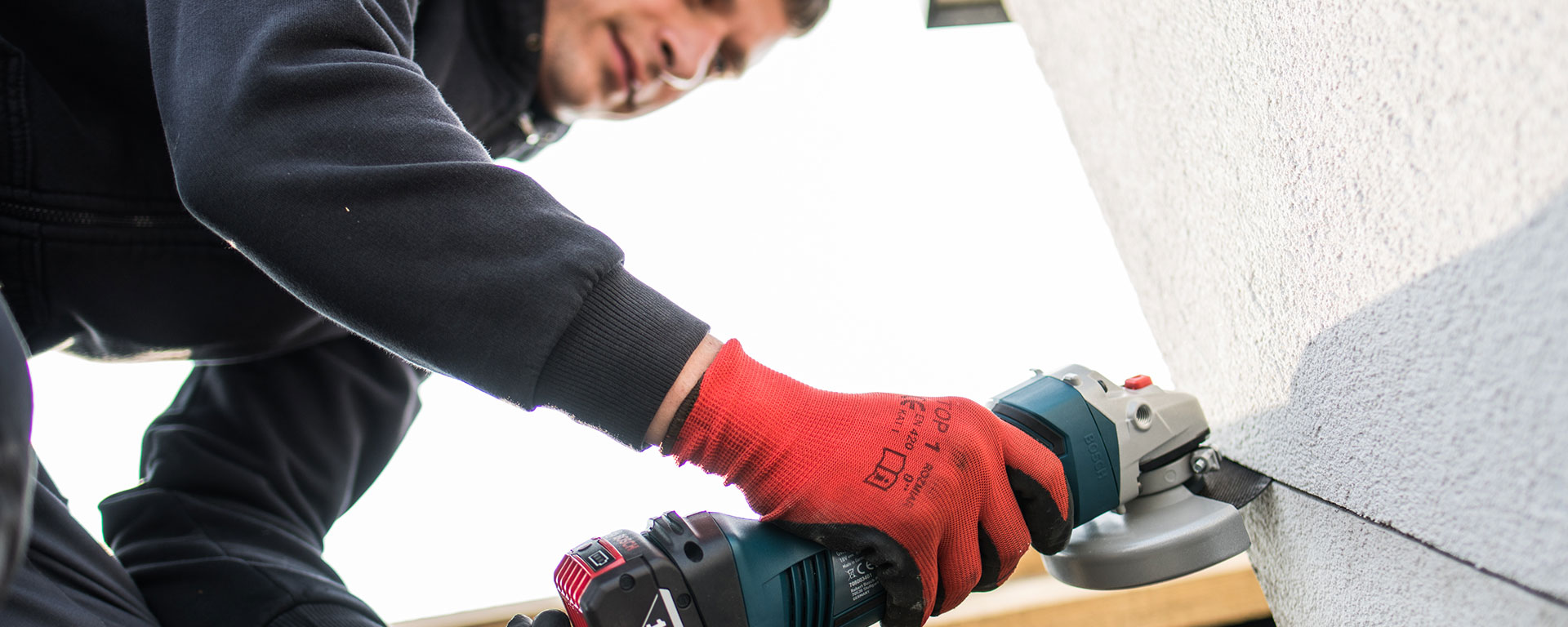 Mężczyzna w czerwonych rękawicach używa szlifierki kątowej Bosch.