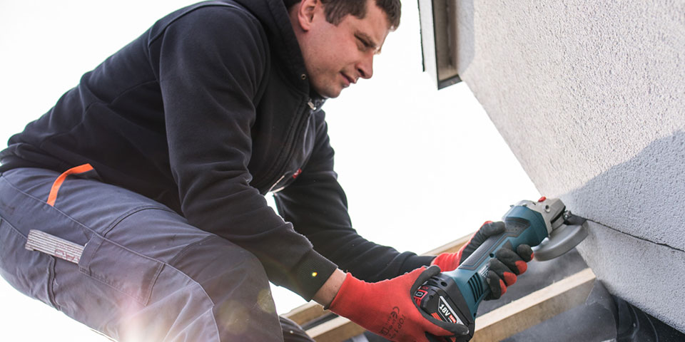 Rzemieślnik w czerwonych rękawicach tnie narzędziem w ścianę.