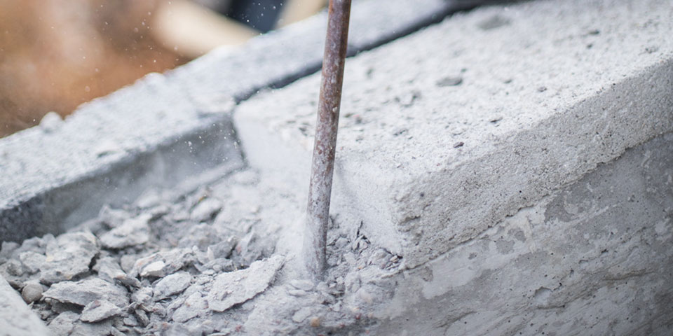 Blok betonowy z prętem stalowym, otoczony zmielonym kamieniem.