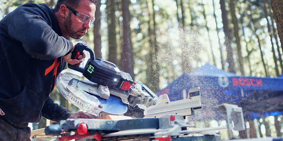 Muž používá pokosovou pilu Bosch Professional v lese, dřevěný prach létá.