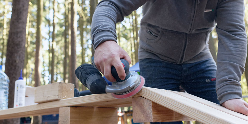 Řemeslník brousí dřevo s nástrojem Bosch v lese.