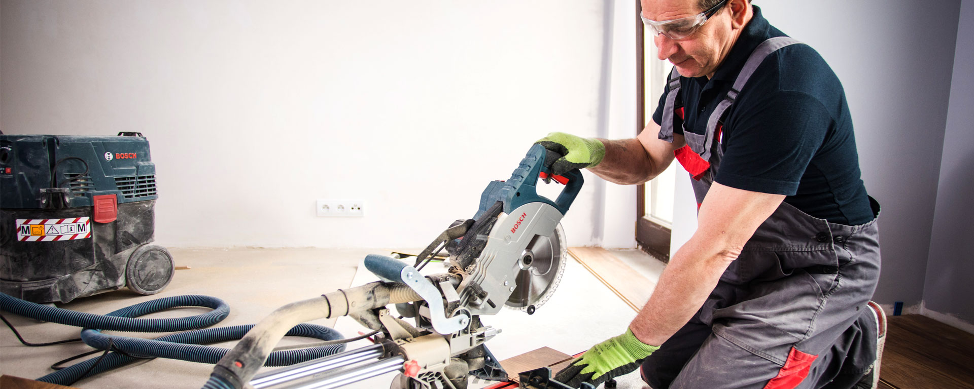Řemeslník používá pokosovou pilu Bosch v místnosti s dřevěnou podlahou.