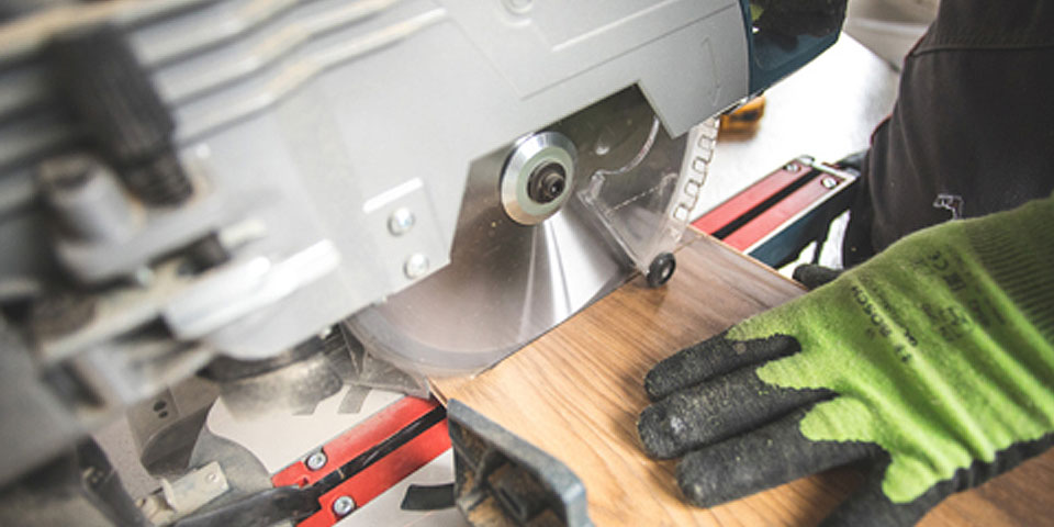 Osoba v zelených rukavicích používá kotoučovou pilu na dřevo.