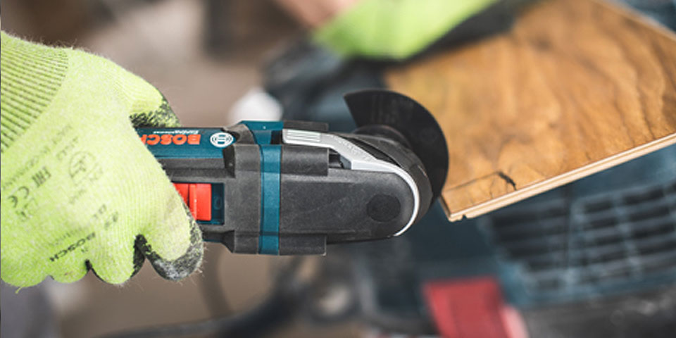 Ruka drží multifunkční nástroj Bosch Professional nad dřevem.