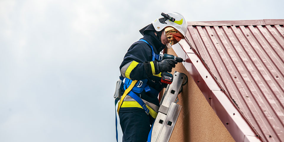 Rzemieślnik w odzieży ochronnej pracuje z wiertarką akumulatorową na dachu.