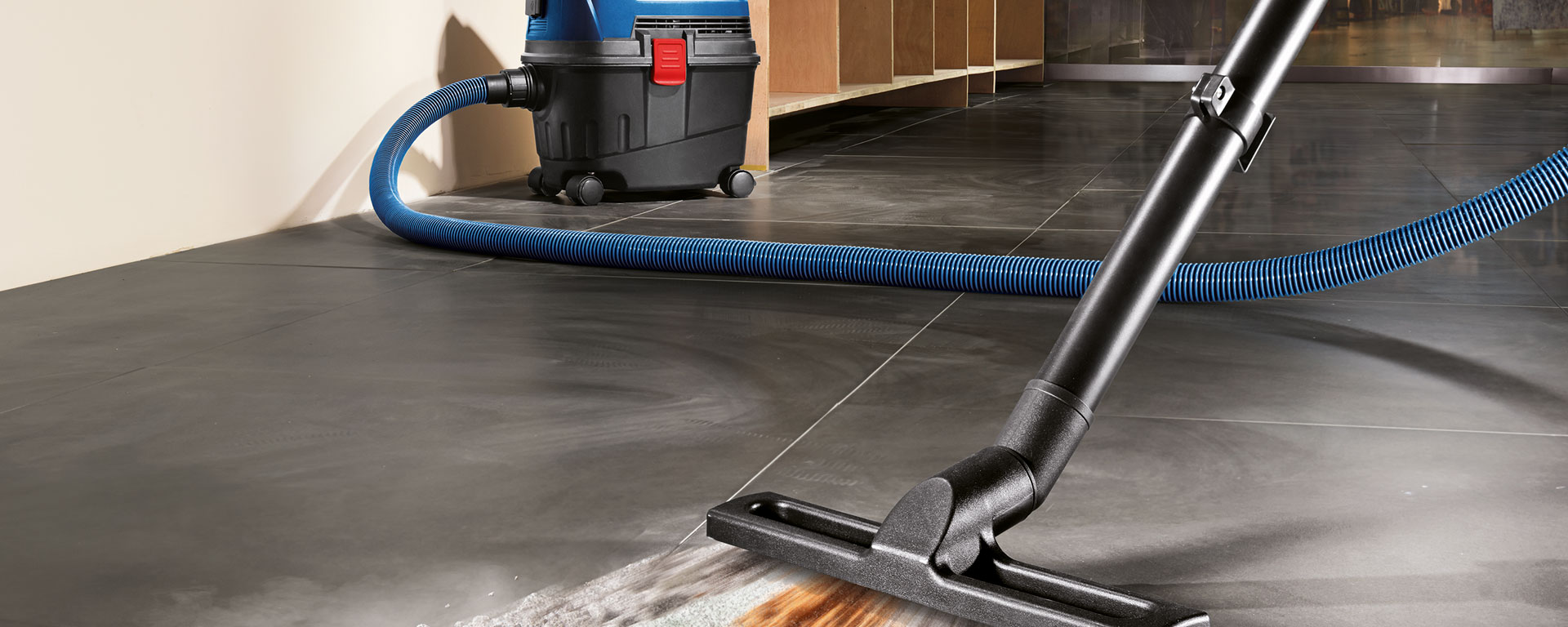 Una aspiradora negra Bosch Professional con una manguera azul sobre baldosas.
