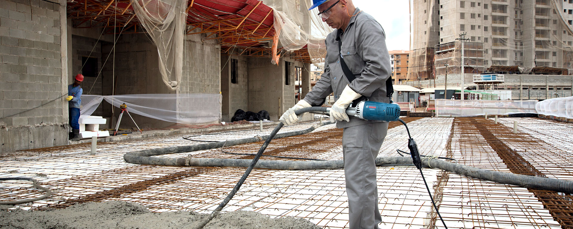 Un trabajador con ropa gris está utilizando un mezclador de concreto Bosch en el sitio de construcción.