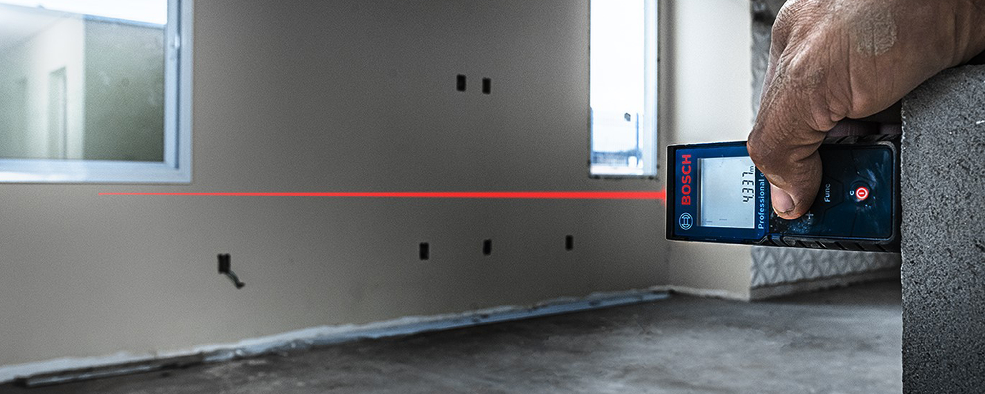 Um medidor de distância a laser Bosch Professional é segurado, laser vermelho visível.