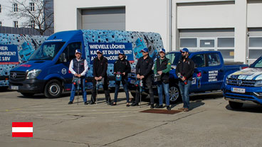 Sechs Personen in einheitlicher Kleidung stehen vor blauen Fahrzeugen.