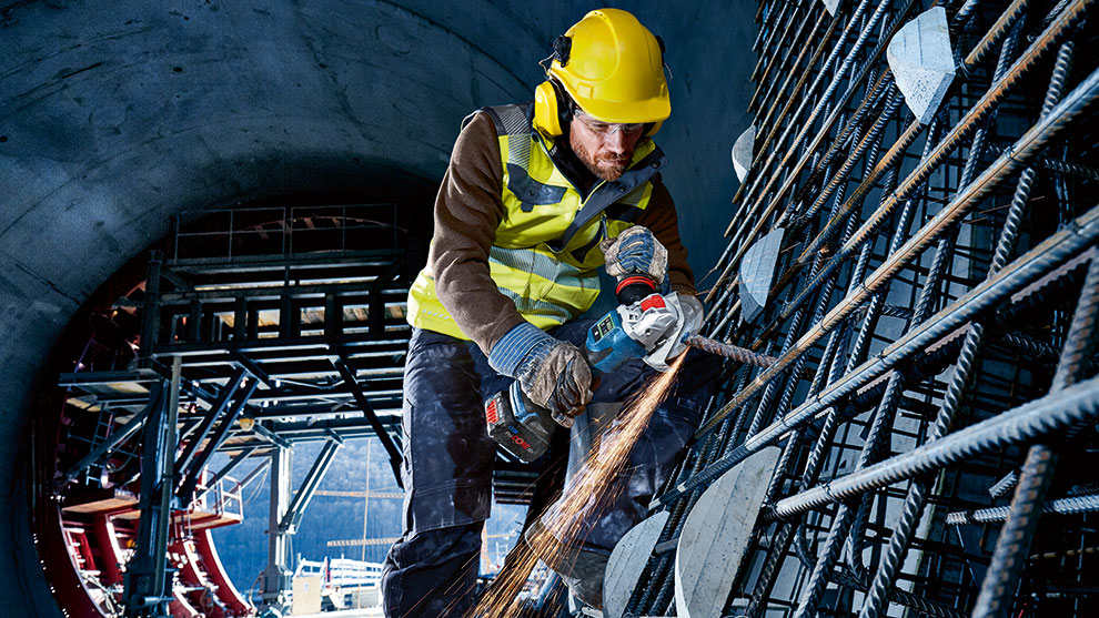 A worker in a helmet is cutting steel with a Bosch Professional machine.