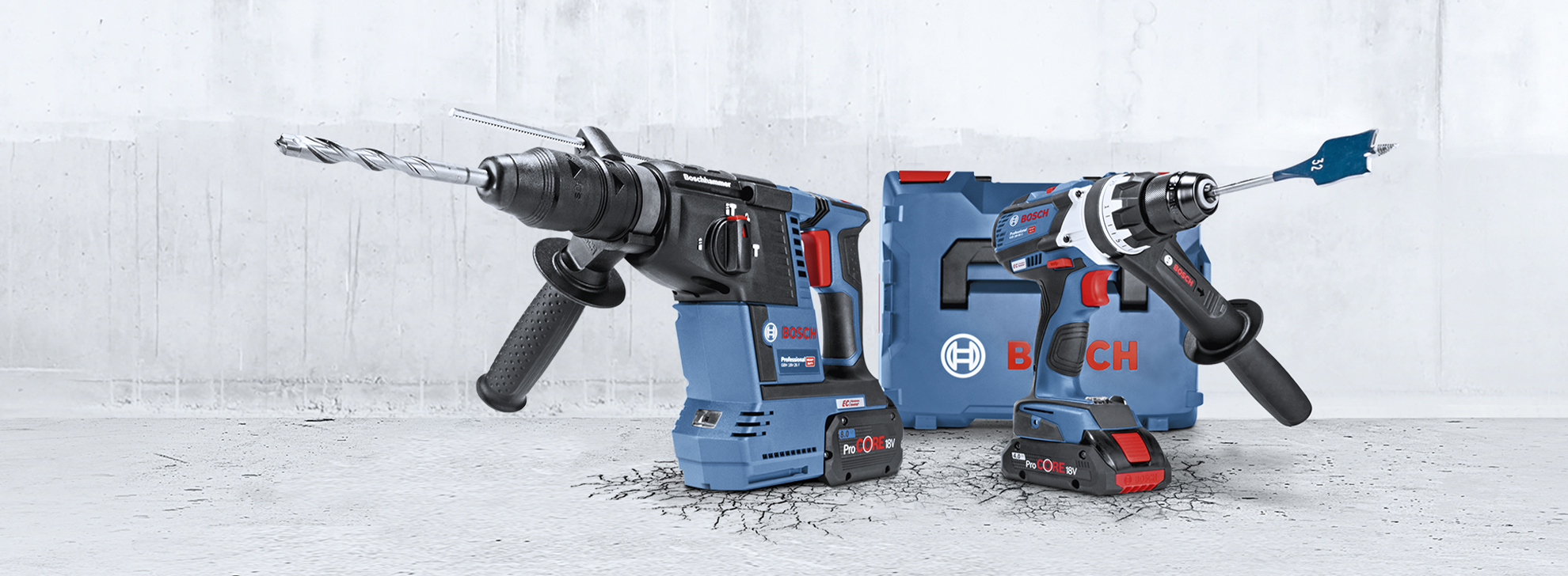 Un martello perforatore Bosch Professional blu e un avvitatore a batteria sono posati su un pavimento grigio screpolato. Accanto a loro c'è una cassetta degli attrezzi blu.