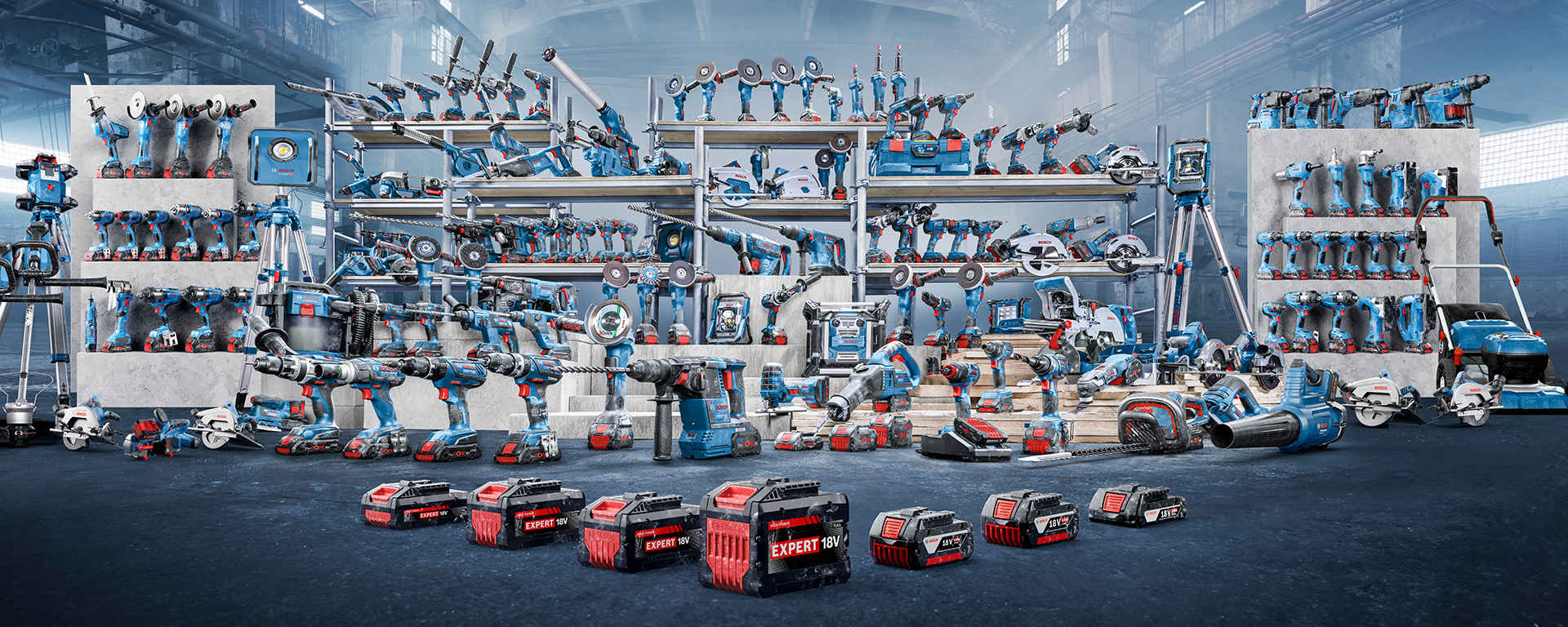 Різноманітні сині інструменти та машини на полицях і підлозі, з червоними акумуляторами на передньому плані.