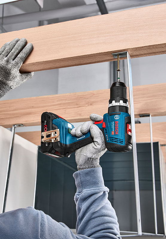 A person wearing gloves is using a blue Bosch cordless screwdriver.