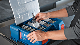 Eine Person öffnet eine blaue Bosch Professional Werkzeugbox mit Einsätzen.