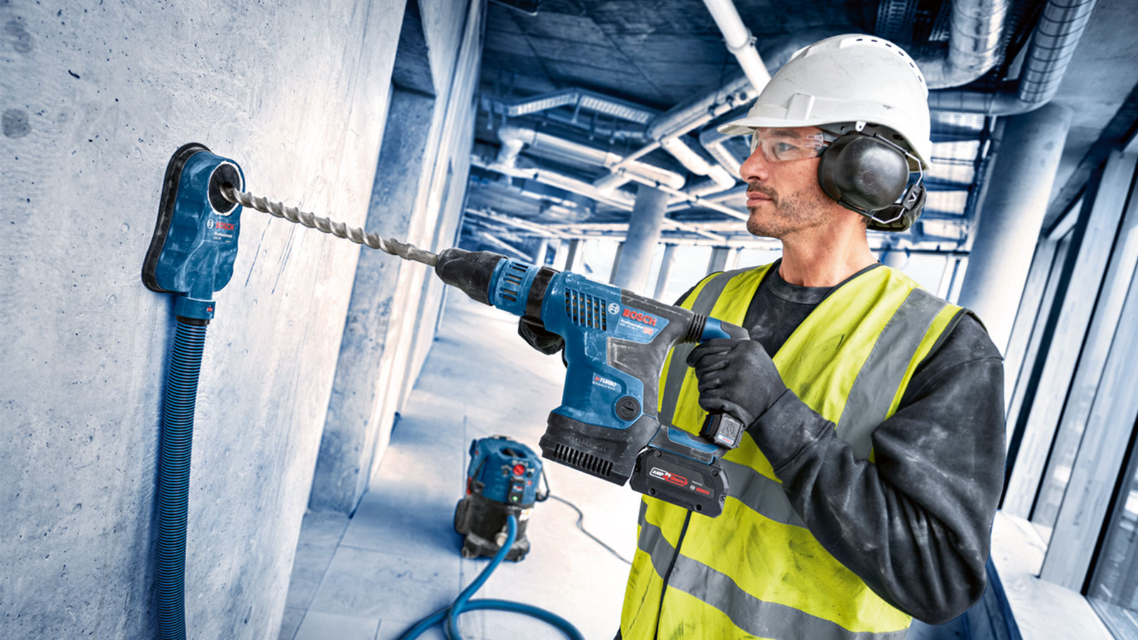 A man with a helmet and safety goggles is drilling into a wall with a blue Bosch drill.