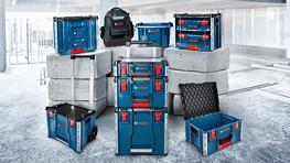 Una disposición de cajas de herramientas azules con acentos rojos sobre un fondo gris, rodeadas de bloques de concreto. Una mochila es visible en el fondo.