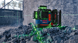 Un proyector de líneas láser verde está sobre escombros grises en una habitación inacabada con paredes en bruto.