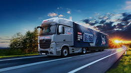 Duży, srebrny ciężarówka jedzie drogą wiejską, otoczony drzewami i czystym niebem.