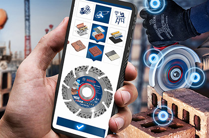 En smartphone med Bosch Professional-appen viser forskellige anvendelser som boring og skæring. I baggrunden ses et værksted med værktøjer og maskiner.