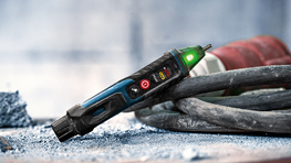 Un appareil de test Bosch Professional avec une lampe LED verte est posé sur de la poussière grise à côté d'un câble noir.