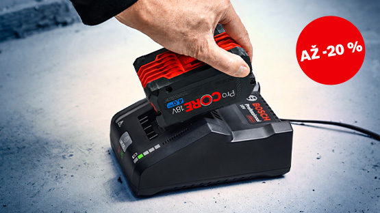 Ruka pokládá červenou baterii Bosch Professional na černou nabíječku, která stojí na šedém podkladu. Je viditelná červená sleva.