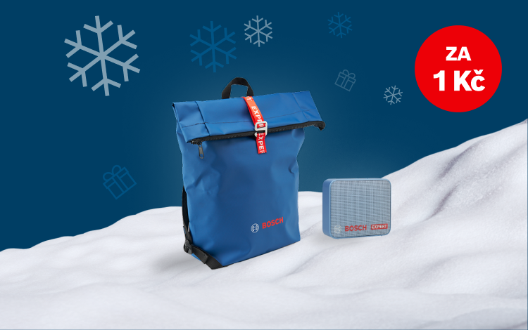 Modrý batoh s červeným uzávěrem a šedé čtvercové zařízení na sněhu. Pozadí je modré.