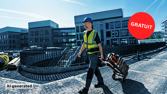 Un ouvrier du bâtiment en gilet de sécurité jaune et casque bleu tire une boîte à outils sur un chantier. En arrière-plan, des bâtiments modernes.
