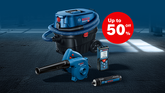 A blue Bosch Professional vacuum cleaner, a blue blower, a measuring device, and a small flashlight on a dark floor. In the background, a discount sign reading "Up to 50% off".