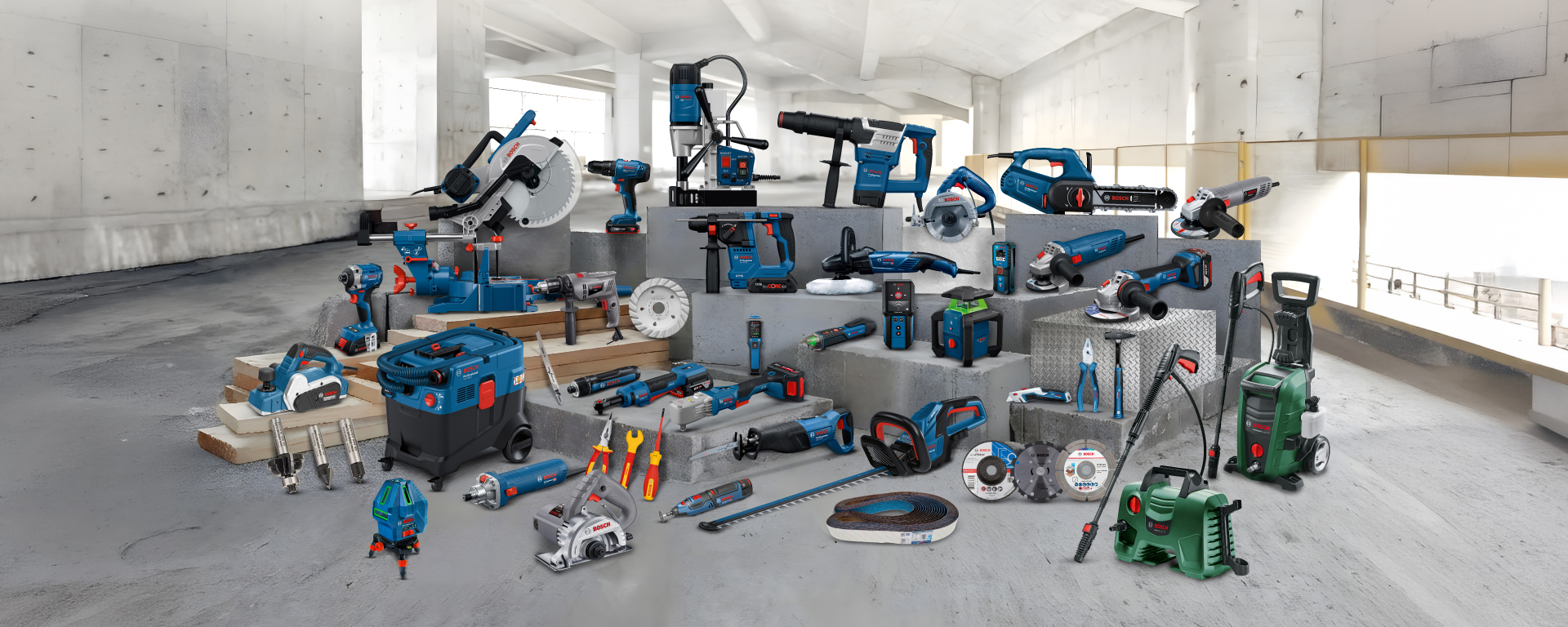 A variety of blue Bosch Professional tools lies on a gray concrete floor, surrounded by wooden planks.