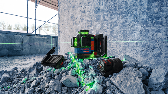 A Bosch Professional line laser stands on a pile of gray stones, surrounded by green laser lines.