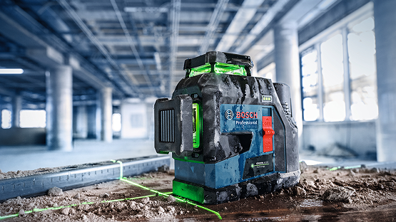 A Bosch Professional line laser stands on uneven ground, surrounded by dust and debris, with green laser lines.