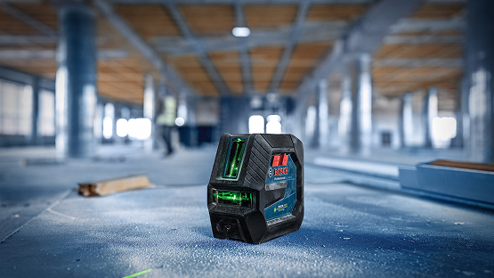 A Bosch Professional line laser stands on a dusty floor in an empty room with wooden columns.