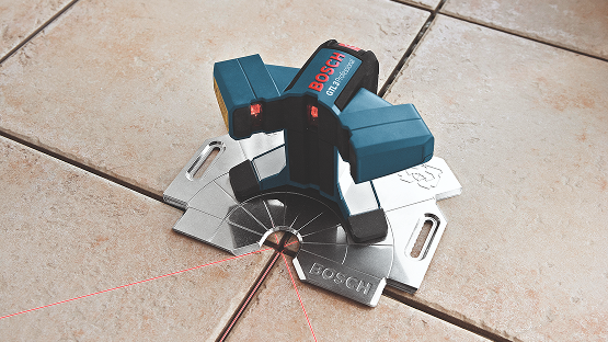 A Bosch Professional line laser stands on a tiled floor, with red laser lines for marking.