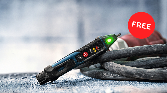 A Bosch Professional voltage tester with green light is lying on a rough surface next to a cable.