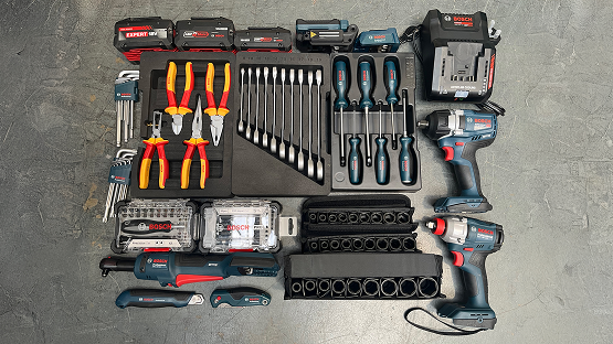 An arrangement of Bosch Professional tools on a gray background: cordless drill, pliers, screwdrivers, bits, and charger, predominantly blue and red.