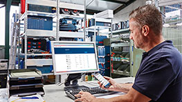 En mand arbejder ved computeren, omgivet af Bosch værktøjer og hylder.